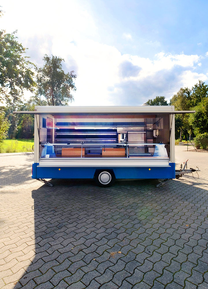 Blauer mobiler Verkaufswagen mit geöffnetem Verkaufsfenster auf gepflastertem Platz im Freien.