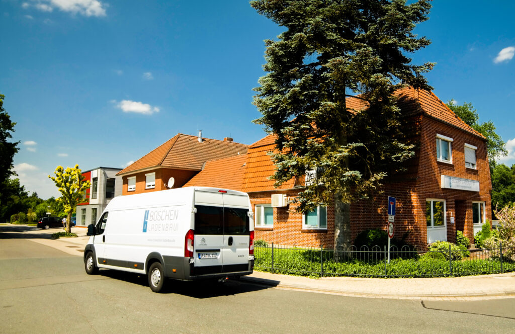 Ansicht Firmengebäude von außen mit Böschen Ladenbau Firmenwagen der daran vorbei fährt.